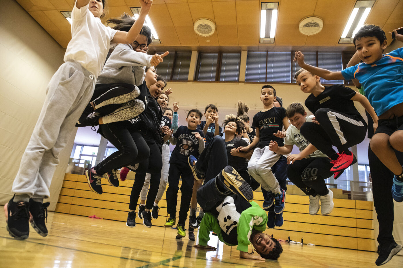 Breakdancer Moses macht einen Breakdance Trick in der Mitte von springenden Kindern.